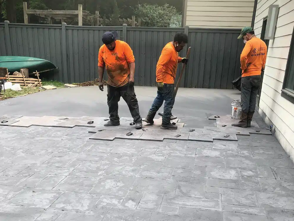 Men in orange shirts installing stamped concrete on outdoor patio.